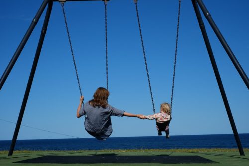 mom and daughter sitting on a park swing